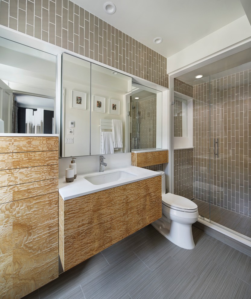 Design ideas for a small modern 3/4 bathroom in Boston with an undermount sink, flat-panel cabinets, medium wood cabinets, solid surface benchtops, an alcove shower, a one-piece toilet, beige tile, ceramic tile, beige walls and porcelain floors.