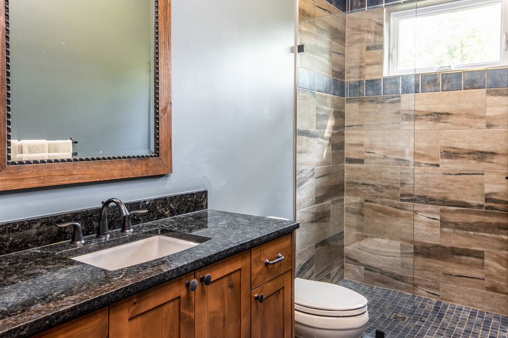 Example of a mid-sized mountain style 3/4 brown tile and porcelain tile alcove shower design with recessed-panel cabinets, medium tone wood cabinets, gray walls, an undermount sink, granite countertops, a hinged shower door and black countertops