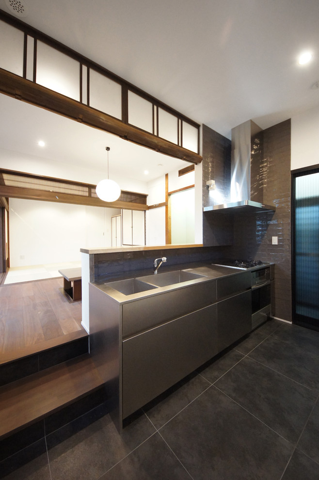 Design ideas for a mid-sized contemporary single-wall open plan kitchen in Tokyo with an integrated sink, flat-panel cabinets, stainless steel cabinets, stainless steel benchtops, grey splashback, matchstick tile splashback, black appliances, slate floors and a peninsula.