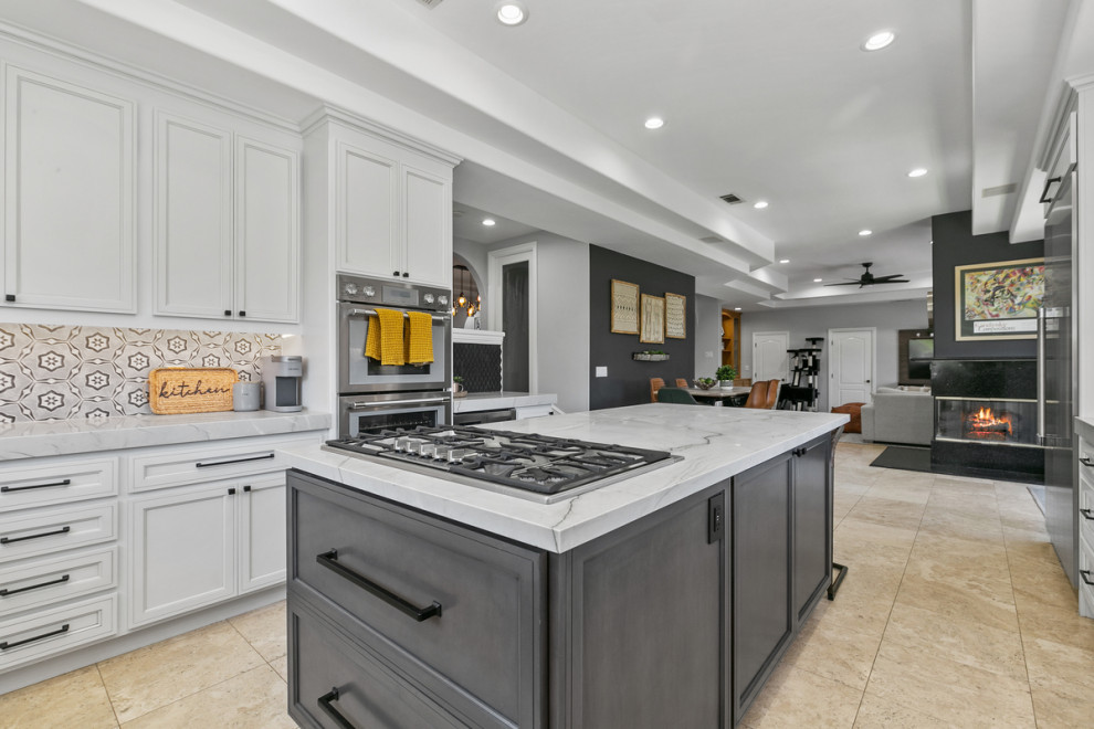 Design ideas for a large transitional u-shaped open plan kitchen in Orange County with a farmhouse sink, shaker cabinets, grey cabinets, marble benchtops, black splashback, ceramic splashback, stainless steel appliances, travertine floors, with island, brown floor, grey benchtop and vaulted.