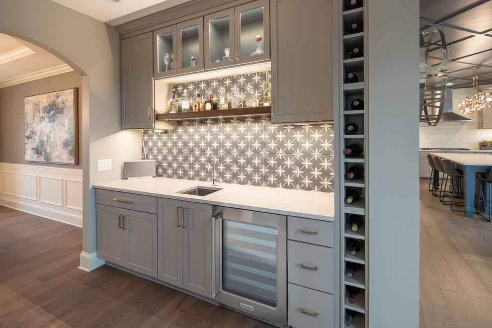 Mid-sized transitional single-wall wet bar in Indianapolis with an undermount sink, shaker cabinets, grey cabinets, grey splashback, cement tile splashback, medium hardwood floors, brown floor and white benchtop.
