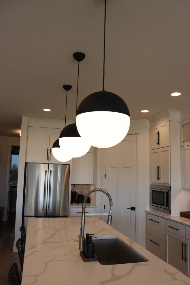 Inspiration for a large transitional l-shaped medium tone wood floor and brown floor open concept kitchen remodel with a single-bowl sink, shaker cabinets, white cabinets, quartz countertops, gray backsplash, subway tile backsplash, stainless steel appliances, an island and white countertops