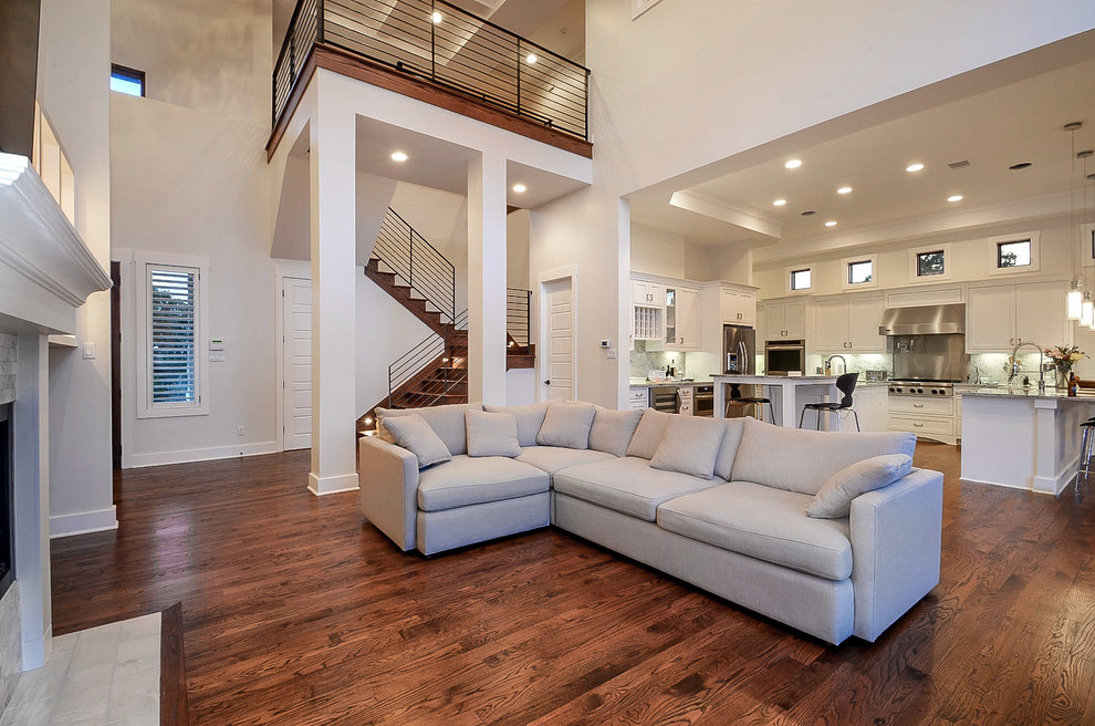 This is an example of a large contemporary open concept family room in Austin with white walls, dark hardwood floors, a standard fireplace, a stone fireplace surround, a wall-mounted tv and brown floor.