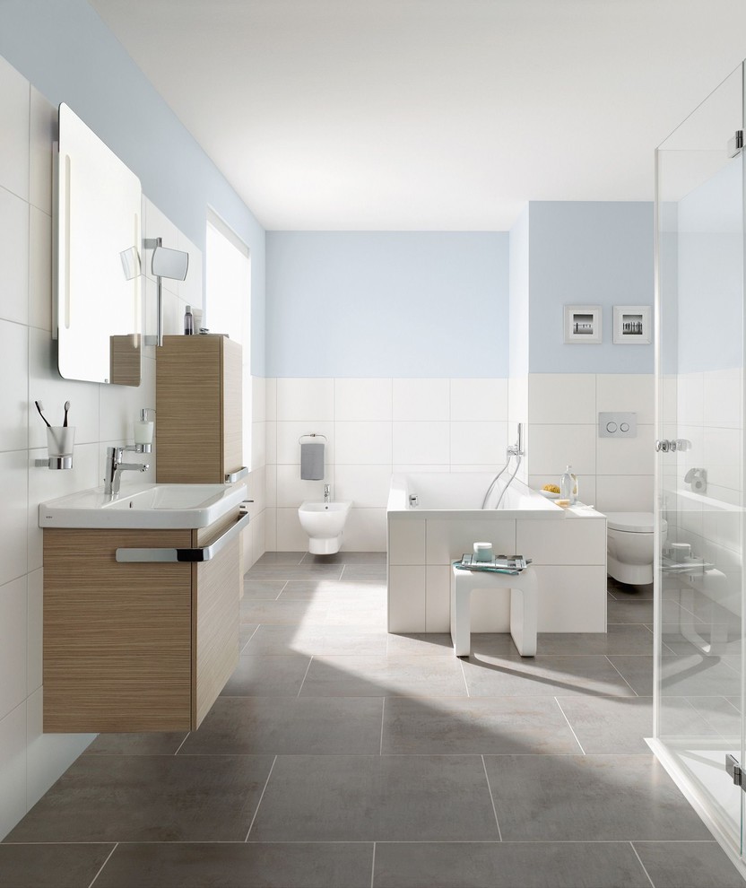 Inspiration for a contemporary bathroom in Frankfurt with flat-panel cabinets, light wood cabinets, a wall-mount toilet, white tile, white walls, a console sink, grey floor, a drop-in tub and wood benchtops.