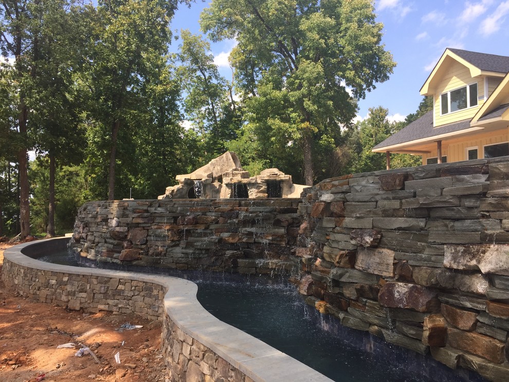 Expansive country backyard custom-shaped infinity pool in Charlotte with a water feature and natural stone pavers.