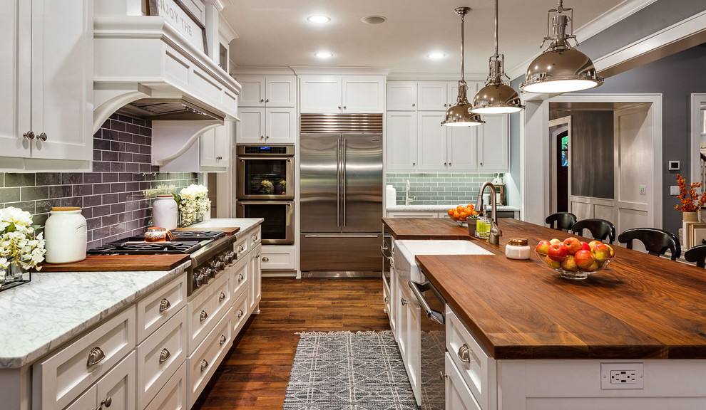 Mid-sized traditional l-shaped open plan kitchen in Kansas City with a farmhouse sink, white cabinets, wood benchtops, grey splashback, ceramic splashback, stainless steel appliances, with island, brown floor, brown benchtop, shaker cabinets and dark hardwood floors.
