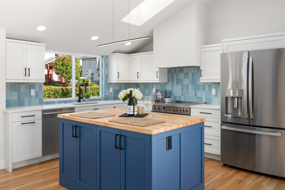 Mid-sized midcentury l-shaped open plan kitchen in Seattle with an undermount sink, shaker cabinets, blue cabinets, wood benchtops, blue splashback, ceramic splashback, stainless steel appliances, medium hardwood floors, with island, brown floor, white benchtop and vaulted.