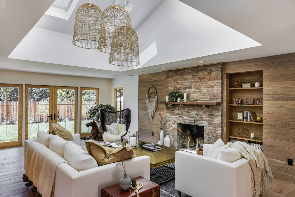 Cette photo montre un salon chic en bois de taille moyenne et ouvert avec un mur blanc, une cheminée standard, un manteau de cheminée en pierre de parement, un sol marron, un plafond voûté et un sol en bois brun.