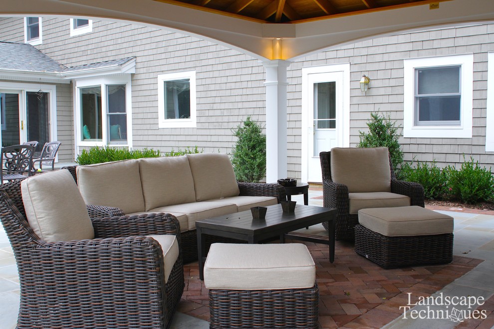 This is an example of a large country backyard patio in New York with a fire feature, natural stone pavers and a gazebo/cabana.