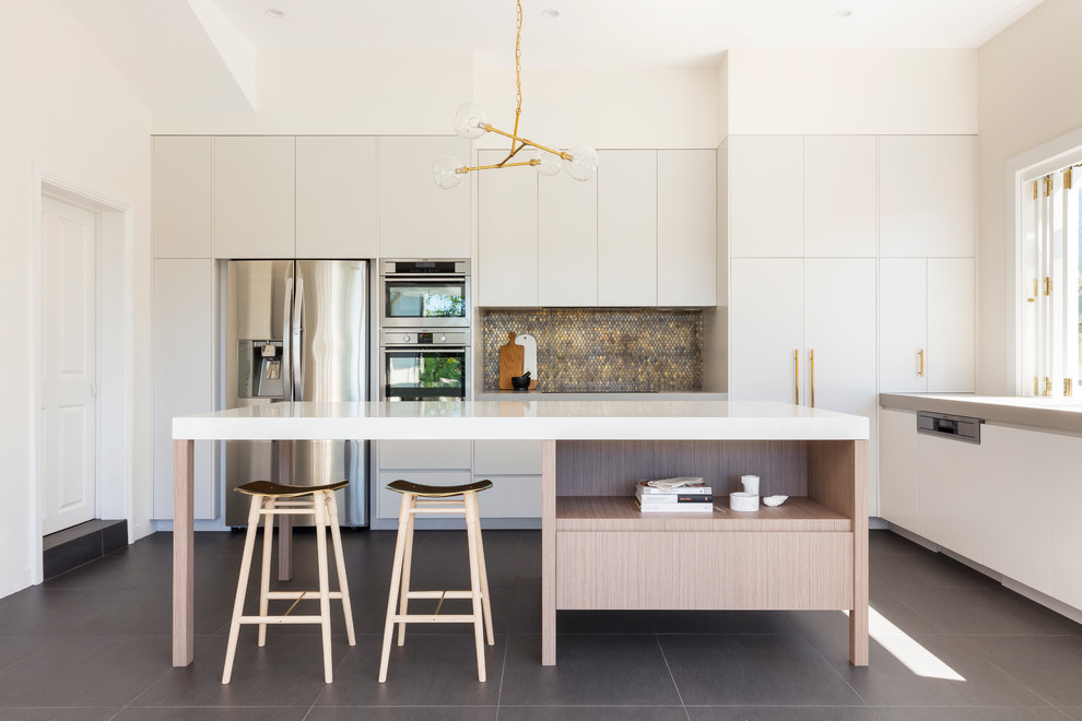 Mid-sized contemporary l-shaped kitchen in Sydney with white cabinets, quartz benchtops, metallic splashback, mosaic tile splashback, stainless steel appliances, slate floors, with island and flat-panel cabinets.
