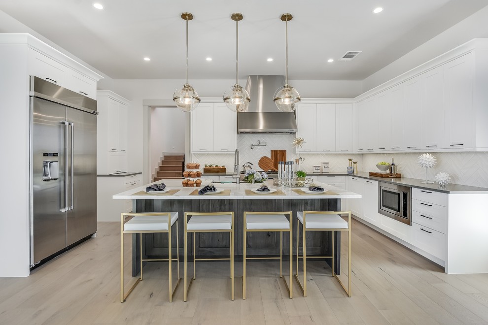 Large trendy u-shaped light wood floor and beige floor kitchen photo in Houston with shaker cabinets, an island, white cabinets, white backsplash, stainless steel appliances and white countertops