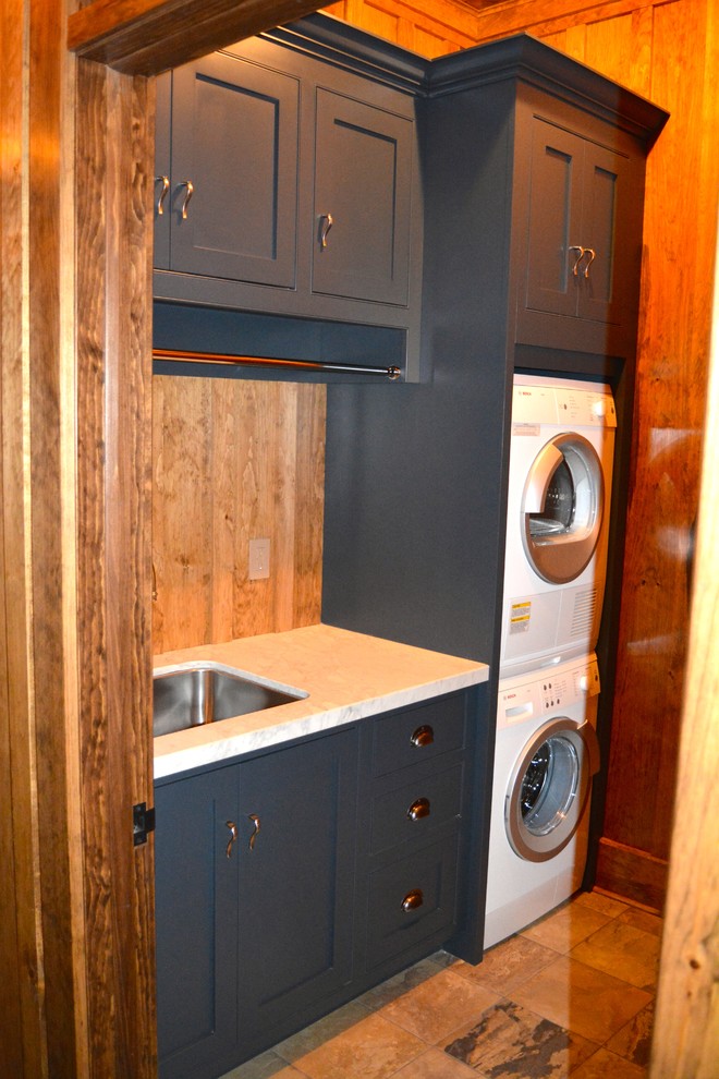 This is an example of a mid-sized country single-wall dedicated laundry room in Toronto with an undermount sink, shaker cabinets, blue cabinets, solid surface benchtops, brown walls, ceramic floors and a stacked washer and dryer.