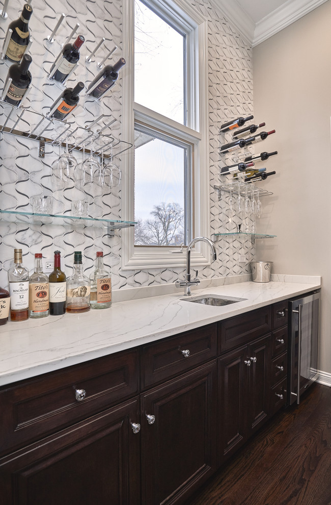 Design ideas for a medium sized traditional single-wall wet bar in Chicago with a submerged sink, recessed-panel cabinets, dark wood cabinets, engineered stone countertops, white splashback, marble splashback, dark hardwood flooring, brown floors and white worktops.