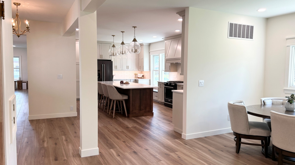 Open concept kitchen - large transitional u-shaped light wood floor open concept kitchen idea with an undermount sink, flat-panel cabinets, white cabinets, quartz countertops, white backsplash, ceramic backsplash, black appliances, an island and white countertops