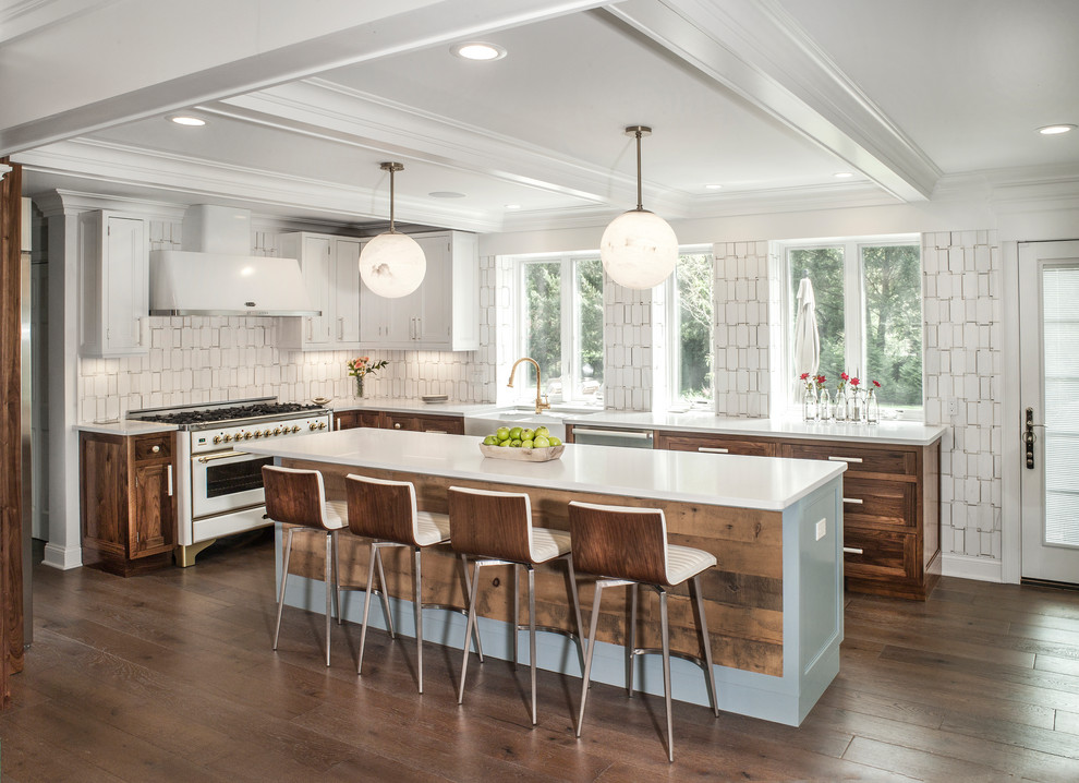Country l-shaped kitchen in New York with a farmhouse sink, shaker cabinets, dark wood cabinets, white splashback, white appliances, dark hardwood floors, with island, brown floor and white benchtop.