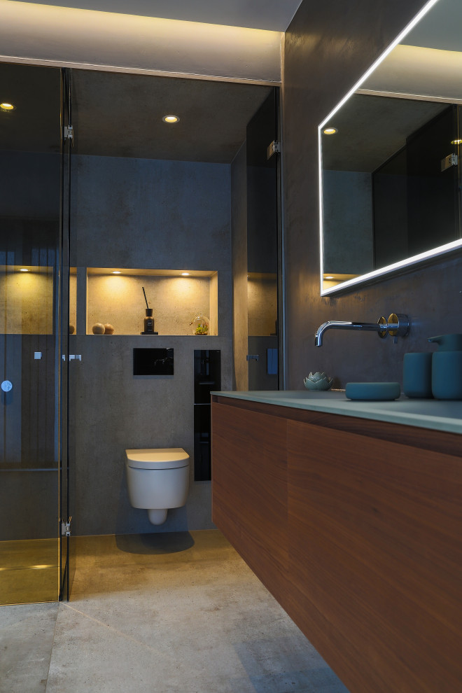 Photo of a large modern master bathroom in Frankfurt with flat-panel cabinets, dark wood cabinets, a drop-in tub, a curbless shower, a wall-mount toilet, gray tile, stone tile, grey walls, cement tiles, an integrated sink, glass benchtops, beige floor, an open shower, green benchtops, a shower seat, a double vanity, a floating vanity, recessed and decorative wall panelling.