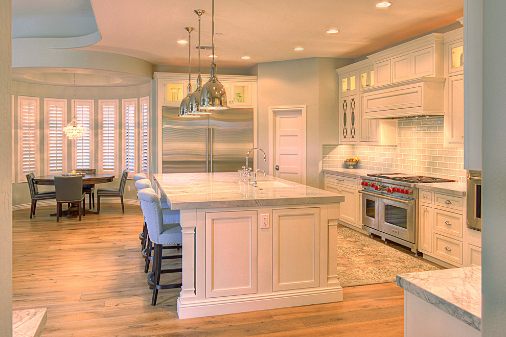 Large transitional l-shaped medium tone wood floor kitchen photo in Phoenix with an undermount sink, recessed-panel cabinets, white cabinets, gray backsplash, subway tile backsplash, stainless steel appliances and an island