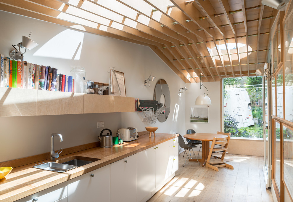 Photo of a contemporary eat-in kitchen in London with flat-panel cabinets, white cabinets, wood benchtops, no island, an undermount sink and light hardwood floors.