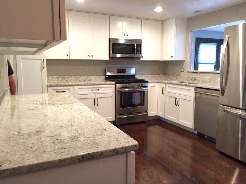 Example of a mid-sized transitional l-shaped dark wood floor eat-in kitchen design with an undermount sink, shaker cabinets, white cabinets, granite countertops, white backsplash, stone slab backsplash, stainless steel appliances and no island