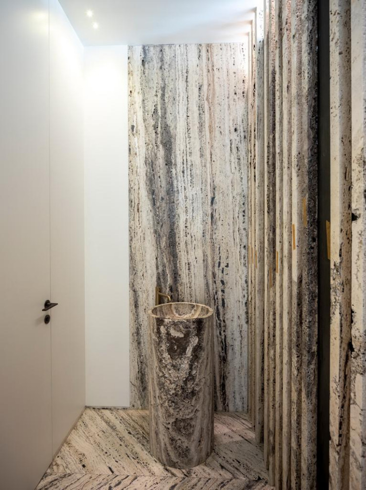 Inredning av ett modernt mellanstort grå grått toalett, med grå skåp, en toalettstol med hel cisternkåpa, svart och vit kakel, travertinkakel, vita väggar, marmorgolv, ett integrerad handfat, bänkskiva i travertin och vitt golv