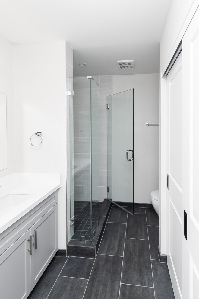 Photo of a beach style master bathroom in San Diego with grey cabinets, ceramic tile, ceramic floors, solid surface benchtops, grey floor, a hinged shower door, white benchtops, a single vanity, a built-in vanity, gray tile and grey walls.