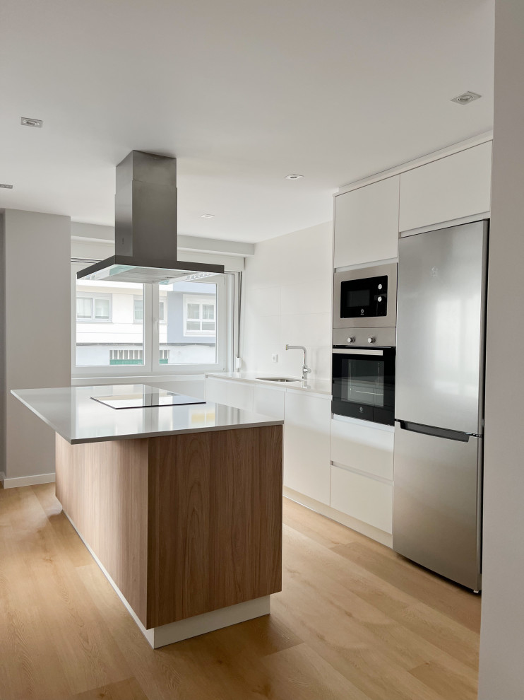 This is an example of a mid-sized scandinavian single-wall open plan kitchen in Other with an undermount sink, flat-panel cabinets, white cabinets, solid surface benchtops, white splashback, ceramic splashback, stainless steel appliances, vinyl floors, with island, brown floor and white benchtop.
