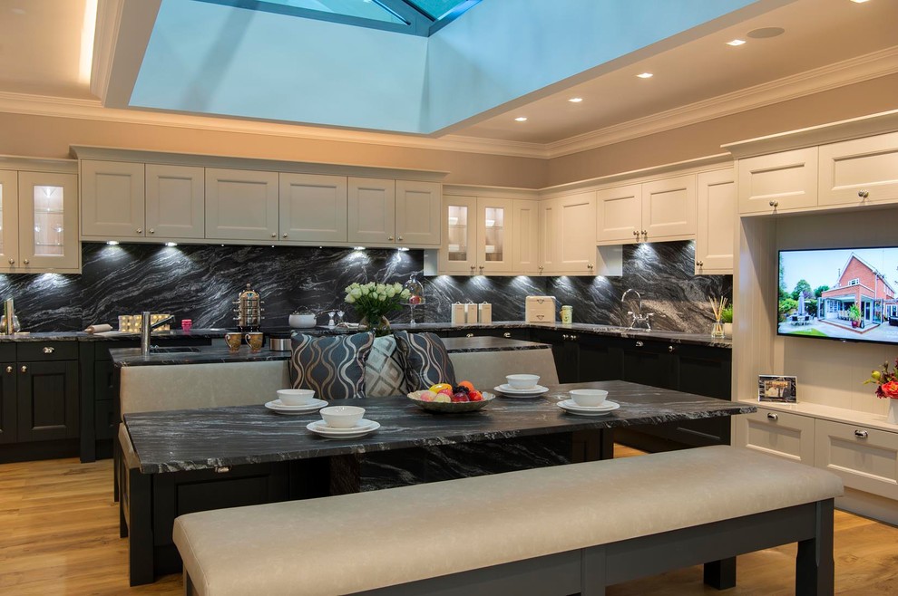 Inspiration for a large contemporary galley eat-in kitchen in Other with an integrated sink, shaker cabinets, grey cabinets, granite benchtops, black splashback, stone slab splashback, black appliances, light hardwood floors, with island, brown floor and black benchtop.