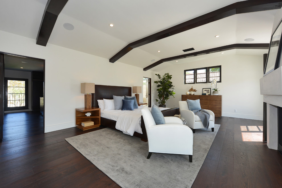 This is an example of a large mediterranean master bedroom in Los Angeles with white walls, dark hardwood floors, a two-sided fireplace, a plaster fireplace surround and brown floor.