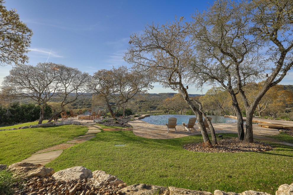 Expansive country backyard full sun garden in Austin with a fire feature and natural stone pavers.