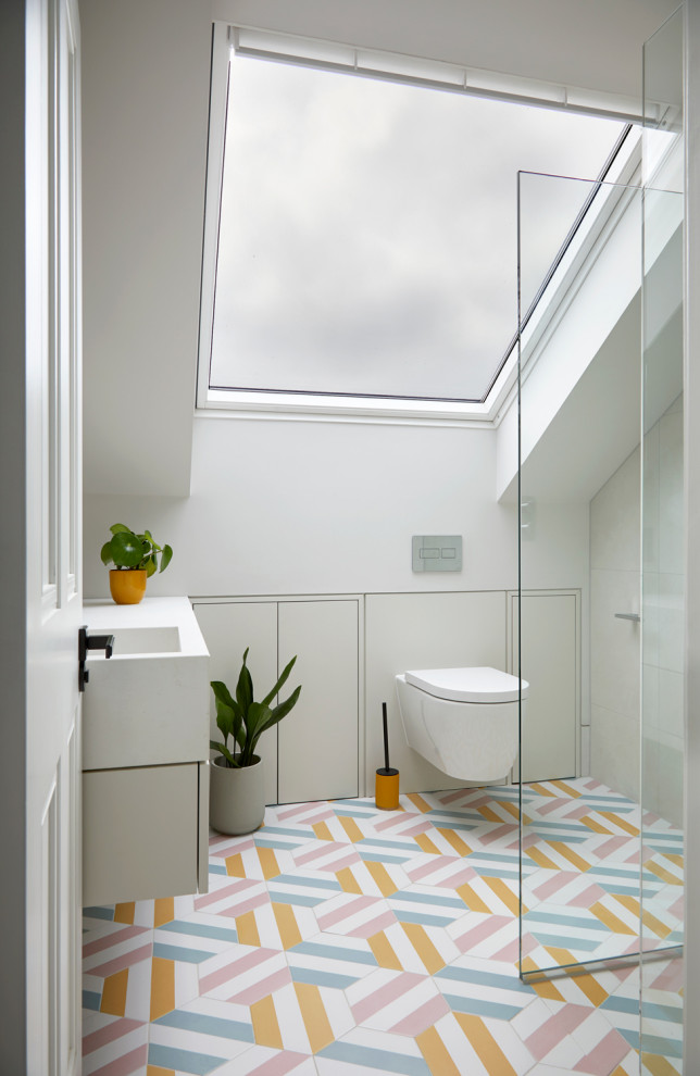 This is an example of a small contemporary family bathroom in London with white cabinets, a corner shower, a wall mounted toilet, beige tiles, ceramic tiles, beige walls, ceramic flooring, a wall-mounted sink, multi-coloured floors, an open shower, a single sink and a floating vanity unit.