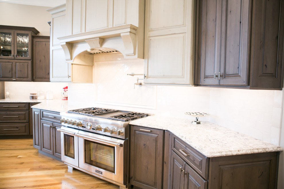 Kitchen - large transitional u-shaped medium tone wood floor and brown floor kitchen idea in Indianapolis with a farmhouse sink, raised-panel cabinets, dark wood cabinets, granite countertops, white backsplash, subway tile backsplash, paneled appliances, an island and multicolored countertops