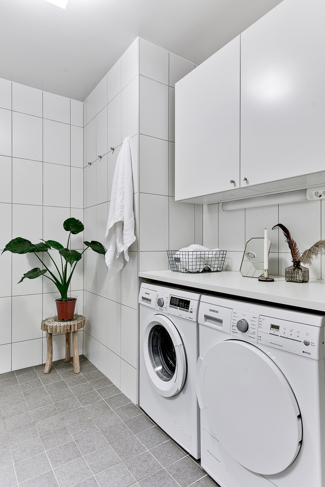 Design ideas for a mid-sized scandinavian single-wall laundry room in Stockholm with flat-panel cabinets, white cabinets, a side-by-side washer and dryer, white walls and ceramic floors.