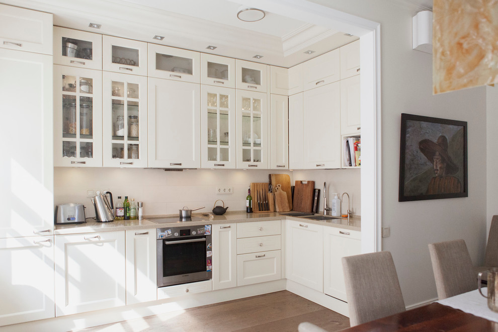 This is an example of a contemporary l-shaped eat-in kitchen in Moscow with a double-bowl sink, recessed-panel cabinets, white cabinets, white splashback, stainless steel appliances and no island.
