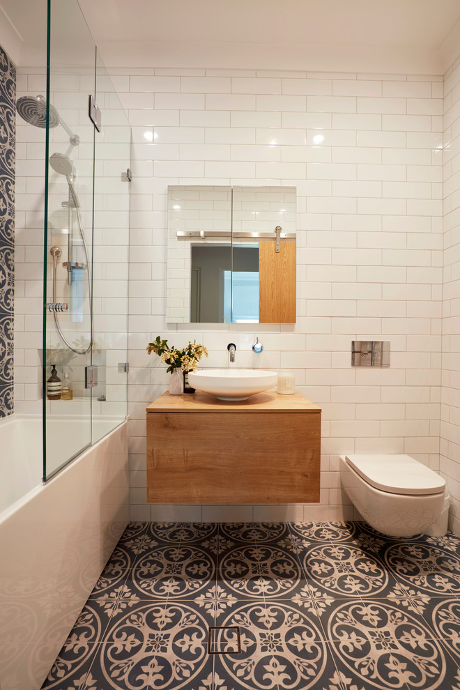 Photo of a small contemporary master bathroom in Sydney with medium wood cabinets, a shower/bathtub combo, a wall-mount toilet, blue tile, white tile, white walls, ceramic floors, a vessel sink, wood benchtops, flat-panel cabinets, an alcove tub, an open shower and brown benchtops.