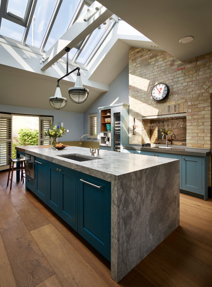 Large transitional u-shaped separate kitchen in London with an undermount sink, recessed-panel cabinets, blue cabinets, grey splashback, stone slab splashback, stainless steel appliances, medium hardwood floors, with island, brown floor and quartzite benchtops.
