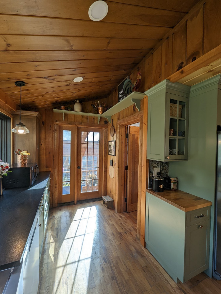 Eat-in kitchen - mid-sized rustic l-shaped medium tone wood floor, brown floor and wood ceiling eat-in kitchen idea with a farmhouse sink, shaker cabinets, green cabinets, granite countertops, multicolored backsplash, ceramic backsplash, stainless steel appliances and black countertops