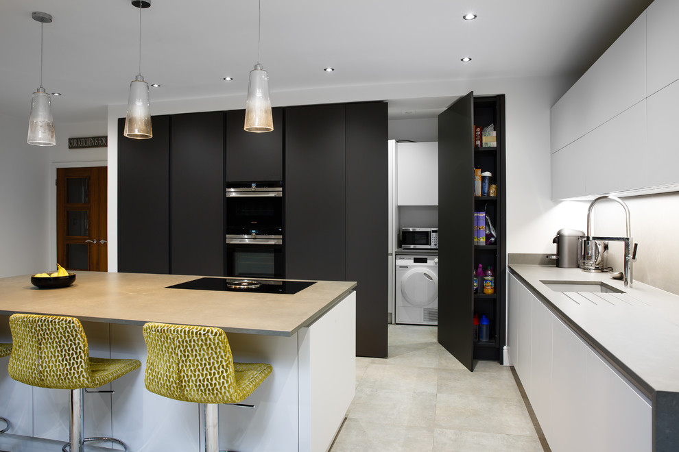 This is an example of a mid-sized modern l-shaped open plan kitchen in Essex with an integrated sink, flat-panel cabinets, grey cabinets, quartzite benchtops, grey splashback, stone slab splashback, panelled appliances, porcelain floors, with island, grey floor and grey benchtop.