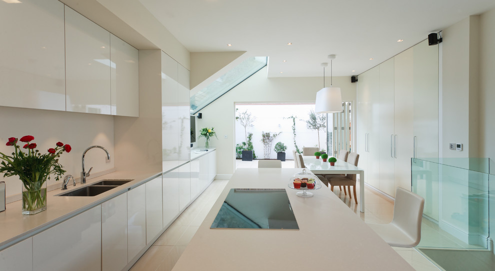 This is an example of a mid-sized contemporary galley eat-in kitchen in London with a double-bowl sink, flat-panel cabinets, white cabinets, white splashback, panelled appliances, quartz benchtops, ceramic floors and with island.