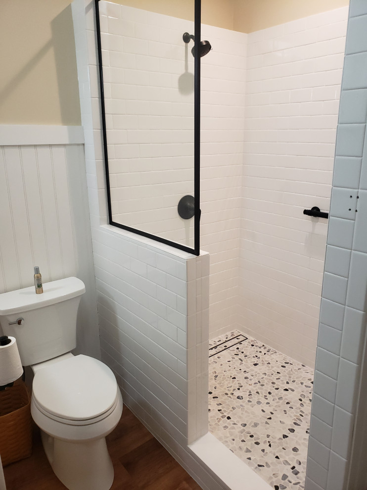 Example of a mid-sized country 3/4 white tile and subway tile vinyl floor, brown floor and double-sink bathroom design in Grand Rapids with shaker cabinets, light wood cabinets, a one-piece toilet, a drop-in sink, granite countertops, black countertops and a freestanding vanity