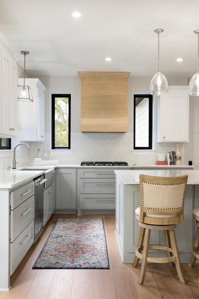 Inspiration for a large transitional l-shaped open plan kitchen in Minneapolis with a farmhouse sink, grey cabinets, quartz benchtops, white splashback, ceramic splashback, stainless steel appliances, medium hardwood floors, with island, brown floor, white benchtop and recessed-panel cabinets.