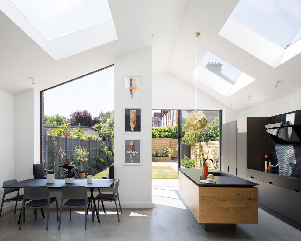 This is an example of a contemporary eat-in kitchen in London with an integrated sink, flat-panel cabinets, black cabinets, concrete floors, with island, grey floor and black benchtop.