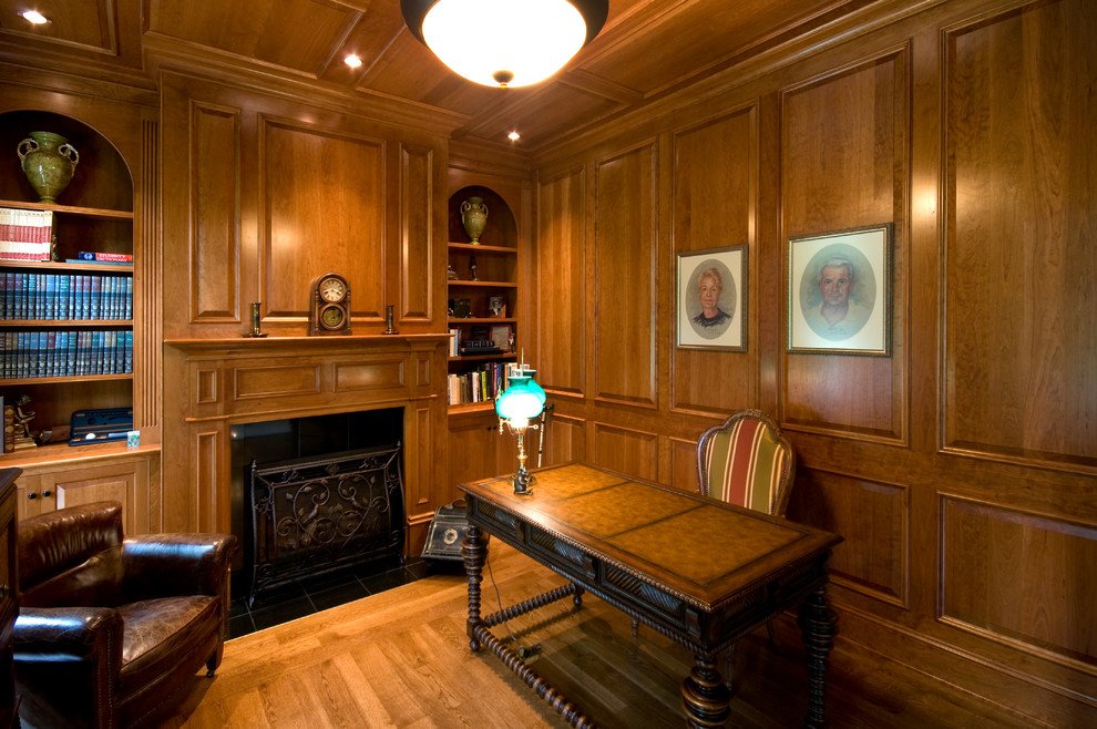 Inspiration for a large traditional home office in Boston with a library, brown walls, dark hardwood floors, a standard fireplace, a wood fireplace surround, a freestanding desk and brown floor.