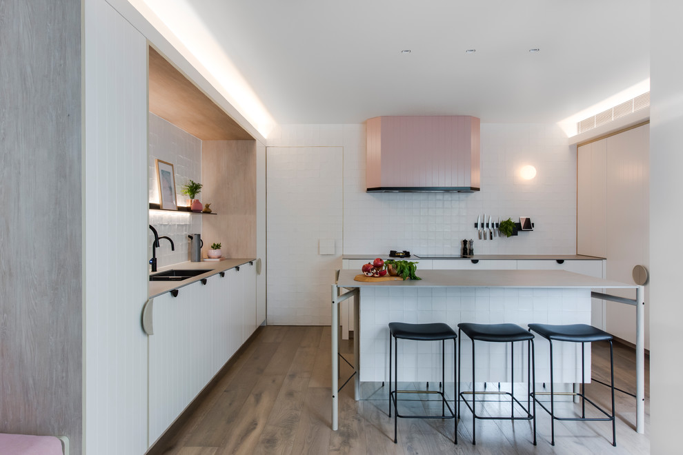 Photo of a mid-sized contemporary l-shaped open plan kitchen in Sydney with a double-bowl sink, white cabinets, recycled glass benchtops, white splashback, cement tile splashback, black appliances, medium hardwood floors, with island, grey benchtop, flat-panel cabinets and brown floor.