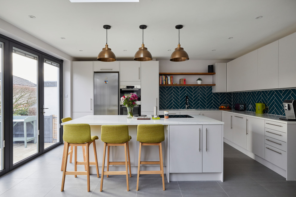 ロンドンにある高級な中くらいなコンテンポラリースタイルのおしゃれなキッチン (アンダーカウンターシンク、フラットパネル扉のキャビネット、シルバーの調理設備、グレーの床、白いキッチンカウンター、グレーのキャビネット、珪岩カウンター、緑のキッチンパネル、セラミックタイルのキッチンパネル、磁器タイルの床) の写真