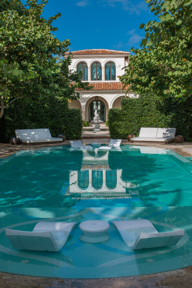 This is an example of an expansive mediterranean round lap pool in Miami with a pool house and natural stone pavers.