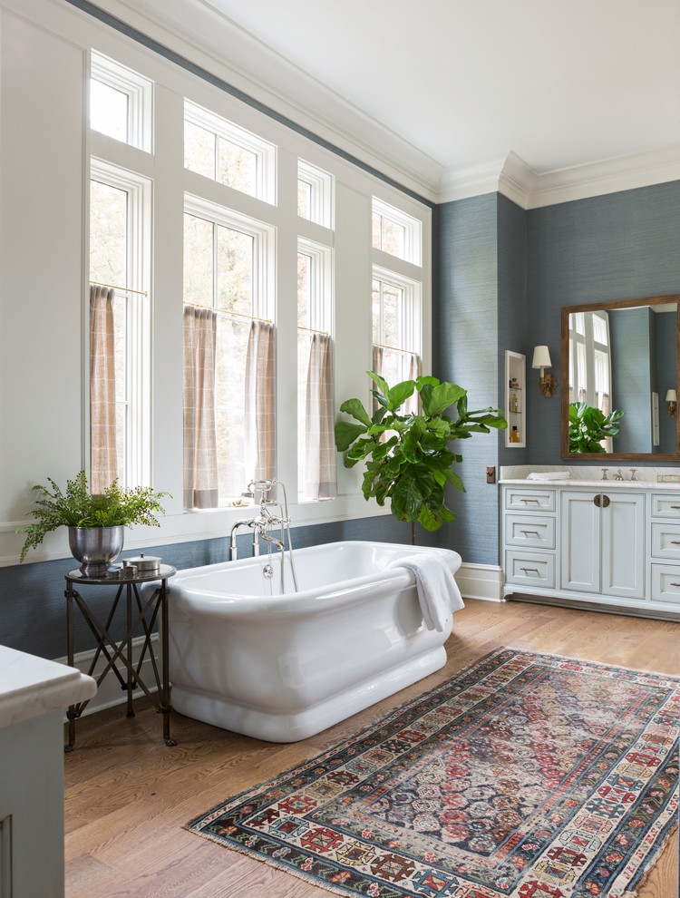 Design ideas for a large tropical master bathroom in Little Rock with a freestanding tub, blue walls, medium hardwood floors, brown floor, white benchtops, shaker cabinets, white cabinets, an alcove shower, granite benchtops and a hinged shower door.