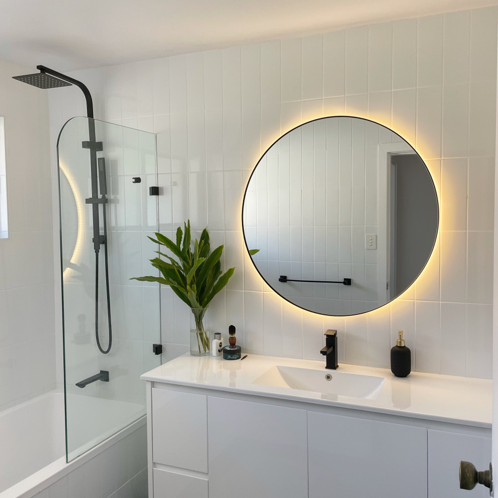 Photo of a modern bathroom in Sydney with white cabinets, a drop-in tub, a shower/bathtub combo, a two-piece toilet, white tile, ceramic tile, white walls, ceramic floors, an integrated sink, engineered quartz benchtops, black floor, an open shower, white benchtops, a single vanity and a freestanding vanity.