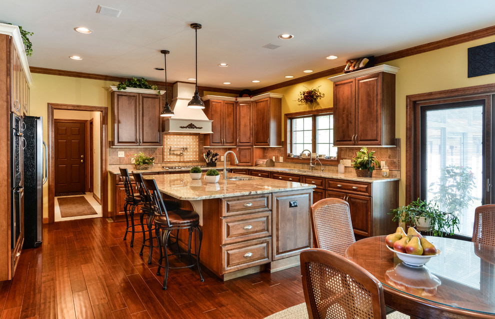 Large transitional u-shaped medium tone wood floor eat-in kitchen photo with beaded inset cabinets, medium tone wood cabinets, granite countertops, beige backsplash, mosaic tile backsplash, stainless steel appliances and an island