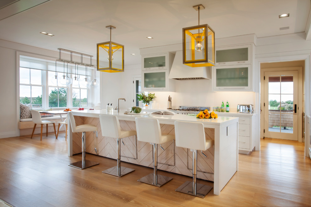 Inspiration for a beach style eat-in kitchen in Boston with glass-front cabinets, white cabinets, white splashback, light hardwood floors, with island and beige floor.