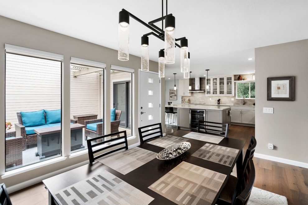 Example of a mid-sized transitional l-shaped medium tone wood floor and brown floor kitchen pantry design with an undermount sink, shaker cabinets, white cabinets, quartz countertops, beige backsplash, subway tile backsplash, stainless steel appliances, an island and beige countertops